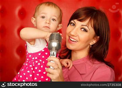 Portrait of mother and doughter with microphone on rack against red wall. Horizontal format.