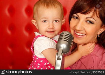 Portrait of mother and doughter with microphone on rack against red wall. Horizontal format. Close up.
