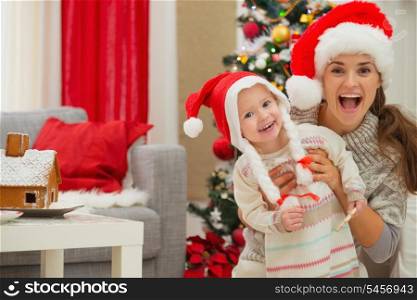 Portrait of mother and eat smeared baby in Christmas hats near Christmas tree