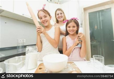 Portrait of mother and two daughters posing on kitchen while cooking