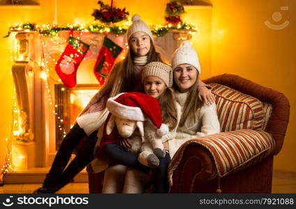 Portrait of mother and two daughters sitting on sofa at fireplace at Christmas eve