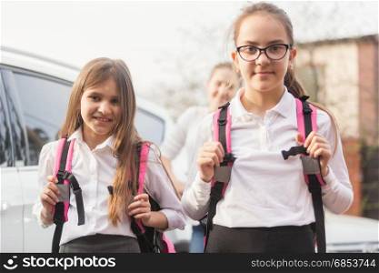 Portrait of mother and two schoolgirls standing at car