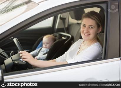 Portrait of mother driving car with little baby boy sitting in safety seat