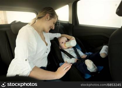 Portrait of mother feeding baby in car safety seat