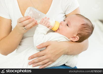 Portrait of mother giving milk from bottle to her baby sleeping on hands