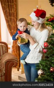 Portrait of mother holding 10 months old baby and decorating Christmas tree