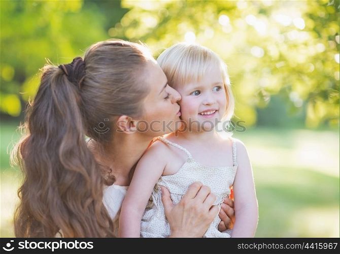 Portrait of mother kissing baby outdoors