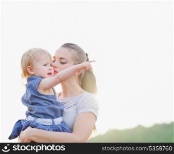 Portrait of mother kissing baby pointing on copy space