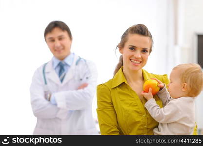 Portrait of mother with baby holding apple and doctor in background