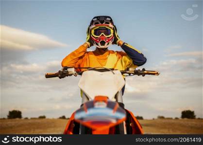 Portrait of motocross rider taking off protective helmet after successful racing. Front view shot. Portrait of motocross rider taking off helmet