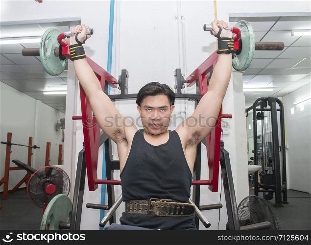Portrait of muscular build athlete exercising on pull down weight machine