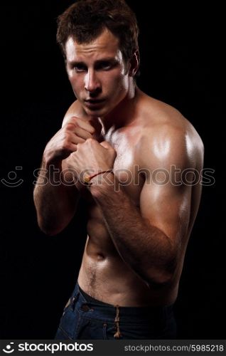 Portrait of muscular man with fighting stance against black background.