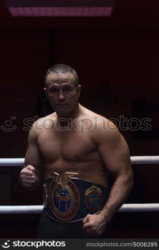 portrait of muscular professional kick boxer with his championship belt in the training ring