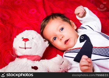 Portrait of newborn boy with blue eyes in her cozy red bed. With teddy bear. Lovely toy