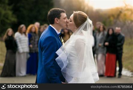 Portrait of newly married couple kissing in front of happy guests at park