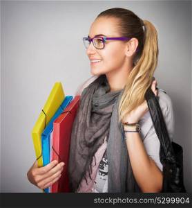 Portrait of nice blond student girl wearing glasses and looking in side, holding in hands folders and bag isolated on gray background