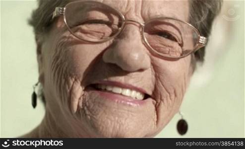 Portrait of old caucasian woman with eyeglasses looking at camera and smiling. Closeup