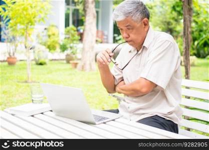 Portrait of old elderly Asian man using a computer laptop in the backyard for learning new skill after retired. Concept of no Ageism and not be late for learning.