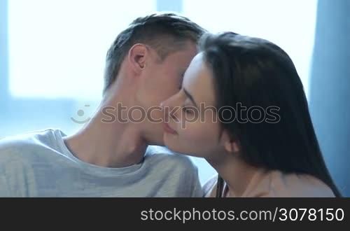 Portrait of passionate couple in love in sensual kiss. Peaceful and tender moments of attractive couple in the bedroom. Attractive loving couple with eyes closed enjoying moments of togetherness with gentle kisses.