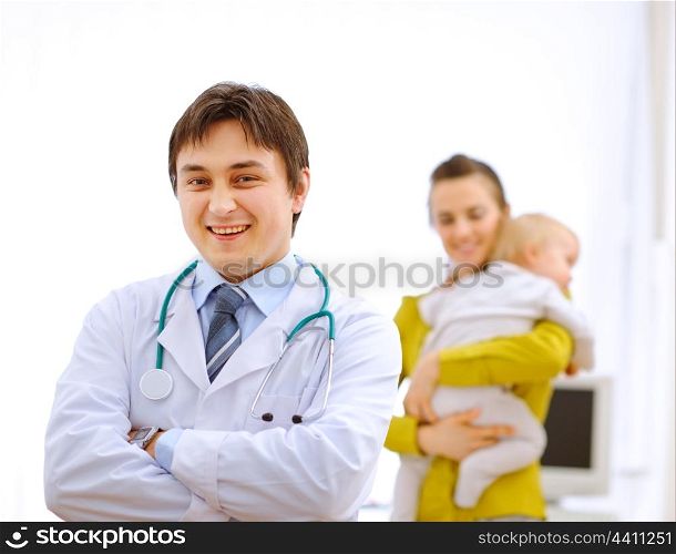 Portrait of pediatrician doctor and mother with baby in background&#xA;