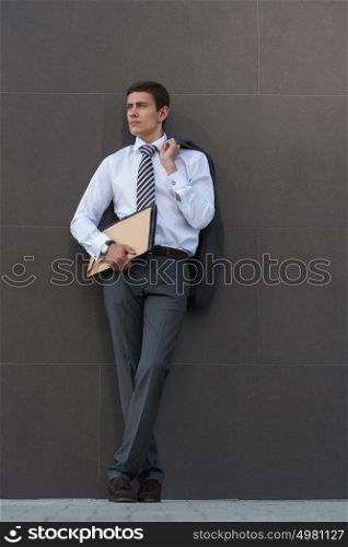 Portrait of pensive and confident adult businessman, wearing suit and necktie with documents in front of gray wall with copyspace