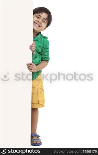 Portrait of playful little boy standing by blank board
