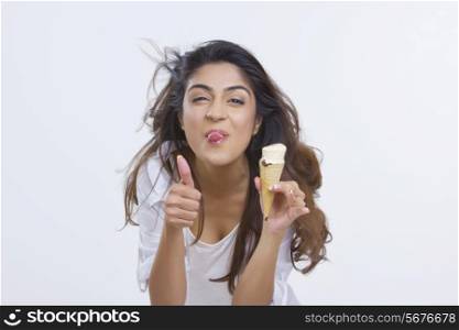 Portrait of playful young woman teasing while holding ice-cream cone over white background