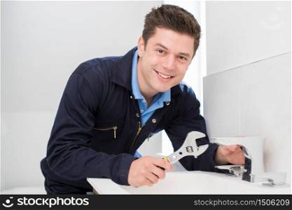 Portrait Of Plumber Working On Sink Using Wrench