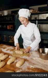 Portrait of positive female baker shaping bread bagels, dipping dough with seeds and oatmeal flakes. Bakery house concept. Portrait of positive female baker shaping bread bagels with seeds