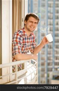 Portrait of positive man drinking coffee on balcony at morning