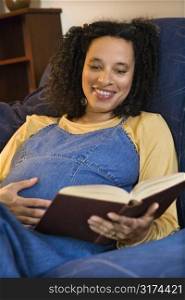 Portrait of pregnant female reading a book and holding her stomach.