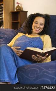 Portrait of pregnant female reading a book and holding her stomach.
