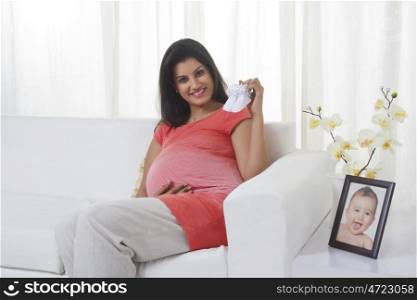 Portrait of pregnant mother holding baby shoes