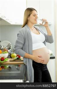 Portrait of pregnant woman drinking water on kitchen