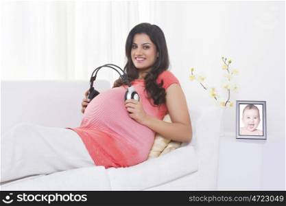 Portrait of pregnant woman putting headphones on her stomach