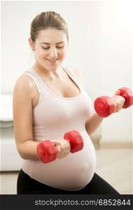 Portrait of pregnant woman sitting on mat and holding dumbbells