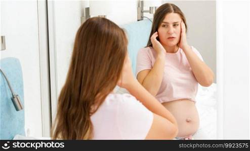 Portrait of pregnant woman suffering from head ache looking in her reflection in mirror. Concept of pregnancy healthcare and medical examination. Portrait of pregnant woman suffering from head ache looking in her reflection in mirror. Concept of pregnancy healthcare and medical examination.
