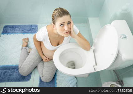 Portrait of pregnant woman with intoxication sitting on floor at toilet