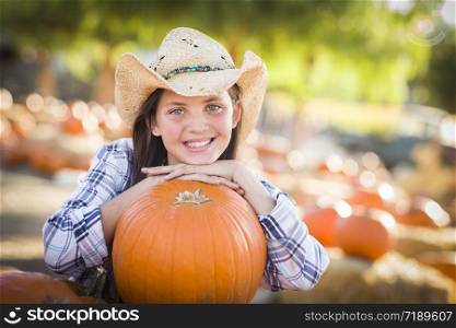 Portrait of Preteen Girl Wearing Cowboy Hat Playing at the Pumpkin Patch in a Rustic Country Setting.