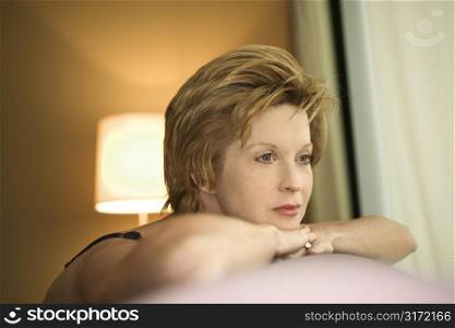 Portrait of pretty Caucasian woman draped over sofa by window looking out.