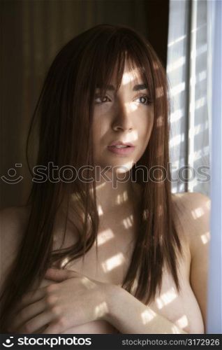 Portrait of pretty Caucasian young woman by sunlit window.