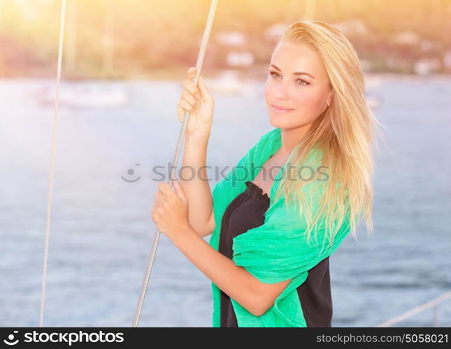 Portrait of pretty dreamy blond girl standing on the deck of luxury sailboat and enjoying beautiful view on sunset, happy summer vacation