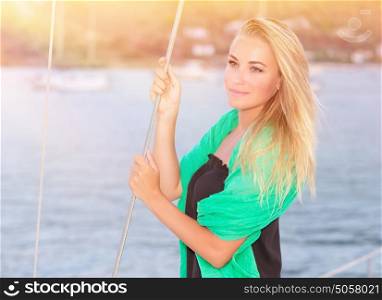 Portrait of pretty dreamy blond girl standing on the deck of luxury sailboat and enjoying beautiful view on sunset, happy summer vacation