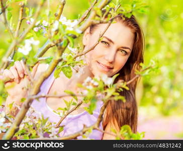 Portrait of pretty girl in spring garden in sunny day, branch of blooming fruit tree, peaceful nature, enjoying spring season
