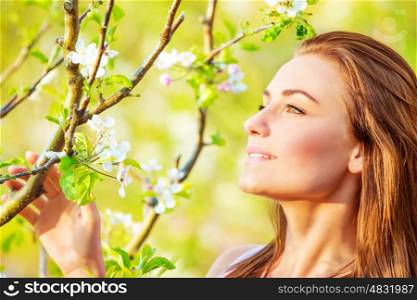 Portrait of pretty girl in spring garden in sunny day, branch of blooming fruit tree, peaceful nature, enjoying spring season