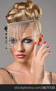 portrait of pretty girl with the elegant hair style and indian decoration on the head, she looks in to the lens and has the right hand near the face