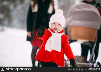 portrait of pretty little girl in red coat enjoying winter day. In the background, her family, mom, dad and little baby brother are in a pram. portrait of pretty little girl in red coat enjoying winter day. In the background, her family, mom, dad and little baby brother are in a pram.