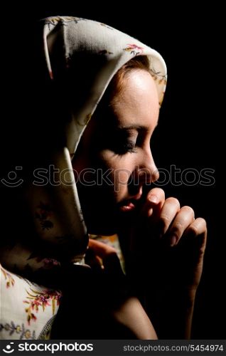Portrait of pretty praying girl with old russian shawl on head on black background. &#xA;