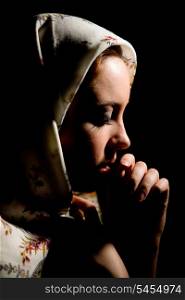 Portrait of pretty praying girl with old russian shawl on head on black background. &#xA;