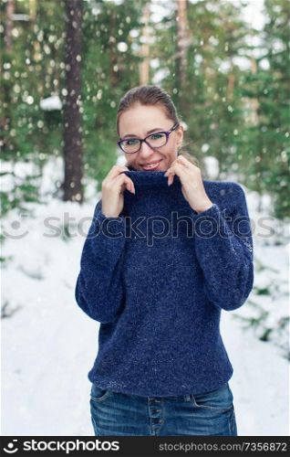 Portrait of pretty woman in a woolen blue sweater in the winter forest. Winter holidays concept or forest walking.. Portrait of pretty woman in a woolen blue sweater in the winter forest